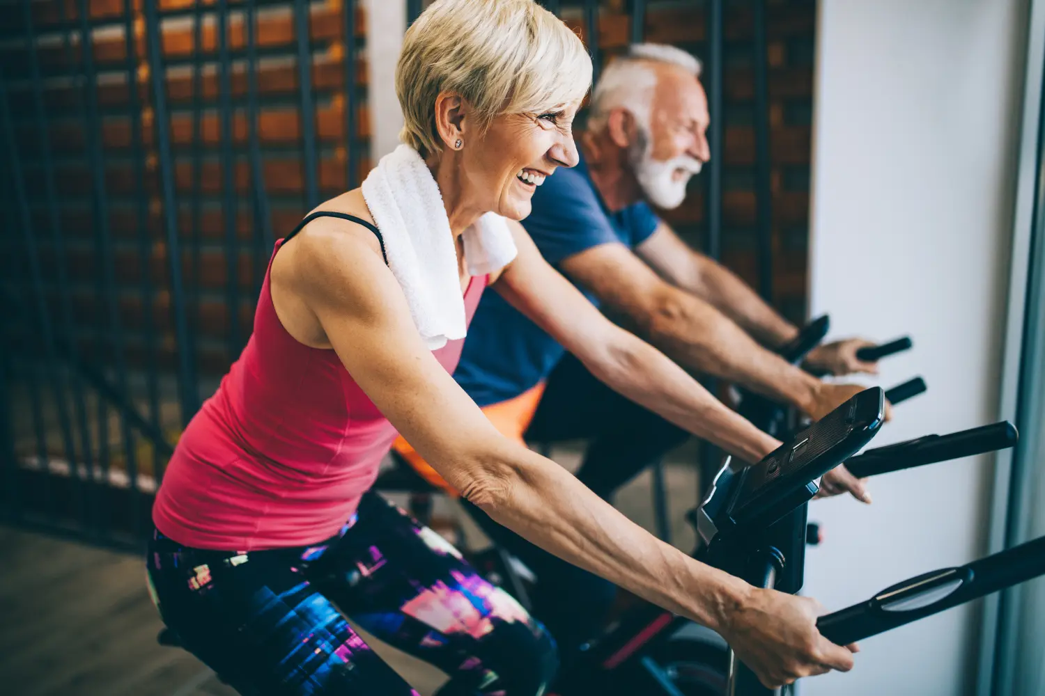 Glücklich fitte reife Frau und Mann, die auf Heimtrainern Rad fahren, um gesund zu bleiben
